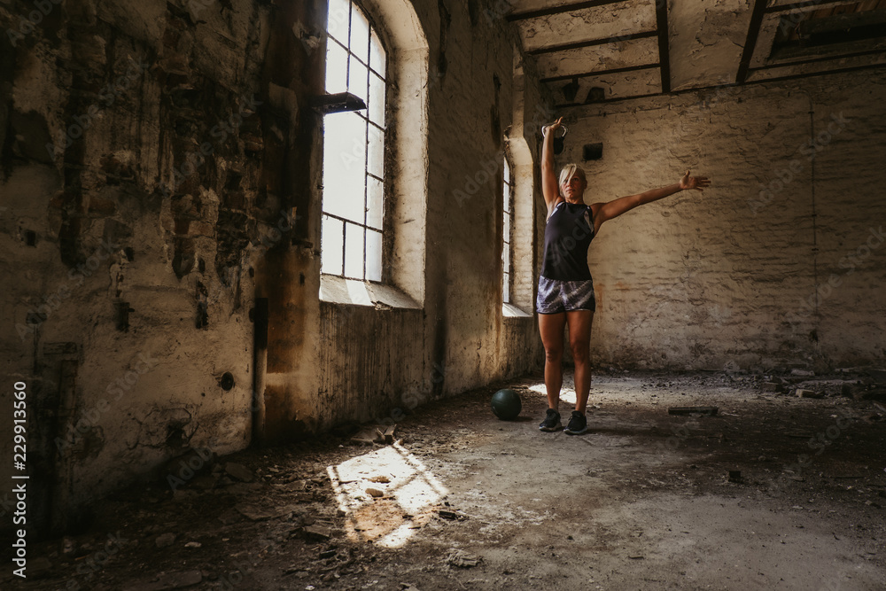 Athletic woman holding kettlebell up in an old building Athletic woman holding kettlebell up in an old building