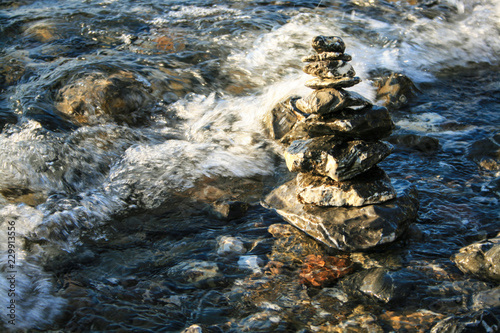 Stone tower in front of the waves. Several stones stand on each other next to the water. Foaming wave approach the stone tower. Sun is reflected in the rolling water again.