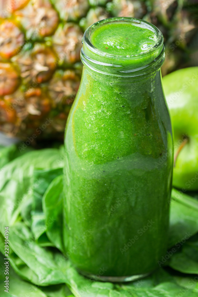 Bottle with Green Fresh Raw Smoothie from Leafy Greens Vegetables Fruits Apples Pineapple Bananas Kiwi Zucchini on Scattered Spinach Leaves. Healthy Lifestyle Detox Vitamins Energy Concept Bottle with Green Fresh Raw Smoothie from Leafy Greens Vegetables Fruits Apples Pineapple Bananas Kiwi Zucchini on Scattered Spinach Leaves. Healthy Lifestyle Detox Vitamins Energy Concept