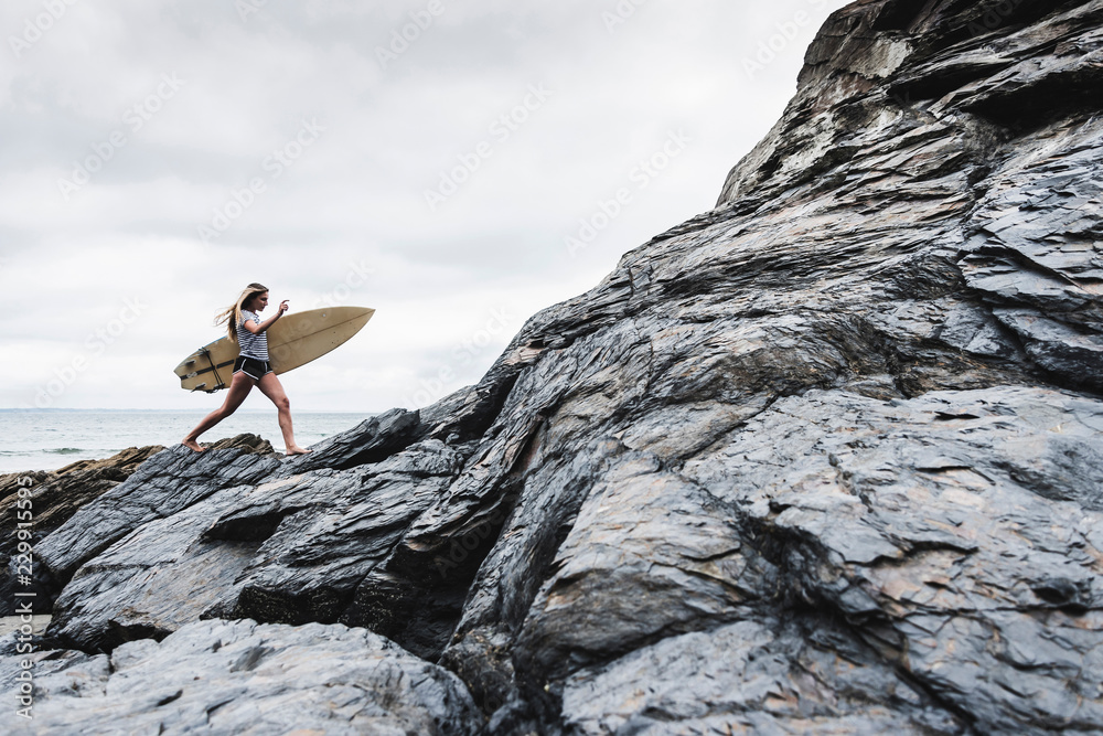 Young woman with surfboard walking on rocks near sea