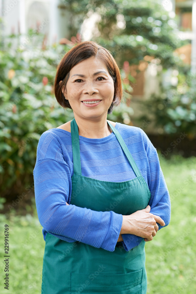 Portrait of mature woman in apron as a gardener standing outdoors and smiling Portrait of mature woman in apron as a gardener standing outdoors and smiling