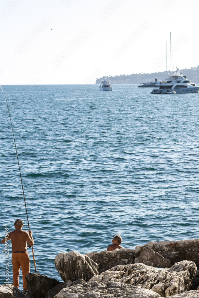 Waterfront of Naples, Italy, september 2017. A couple of old fishermen enjoys the perfect sunny weather to catch some fish in the quiet and relaxing water of the bay of the city. 