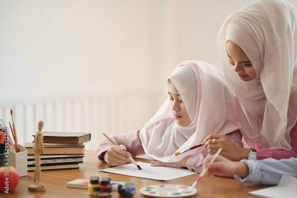 Young Asian Muslim Hijab teaching her student to painting in her art class Young Asian Muslim Hijab teaching her student to painting in her art class