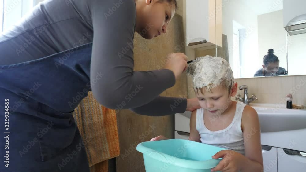 Young mother shaves head of blond boy with razor for preventing pediculosis. Good family tradition. Child is happy from hygiene procedures.