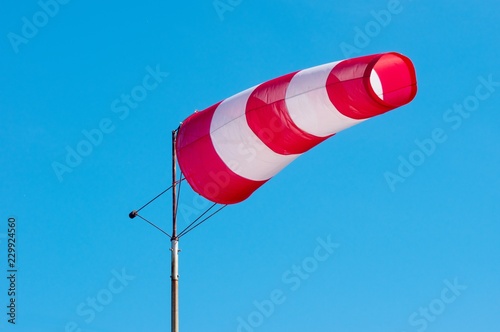 Windsock on blue sky background. Red and white stripe textile in wind with slightly cloudy sky. Indicating direction and speed of wind.