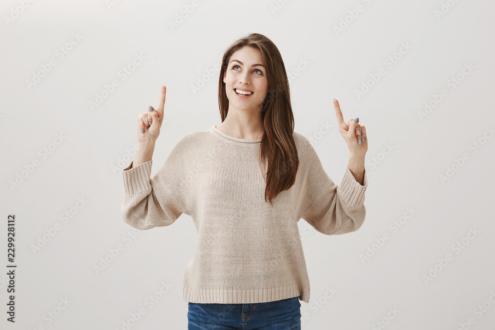 Interesting, where this plane is heading. Studio shot of dreamy charming woman in casual outfit pointing and looking up, smiling broadly, using imagination to picture her vacation over gray wall Interesting, where this plane is heading. Studio shot of dreamy charming woman in casual outfit pointing and looking up, smiling broadly, using imagination to picture her vacation over gray wall