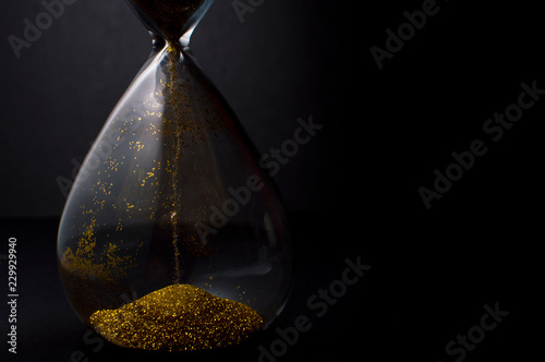Fotografie Sand and golden glitter passing through the glass bulbs of an hourglass measurin