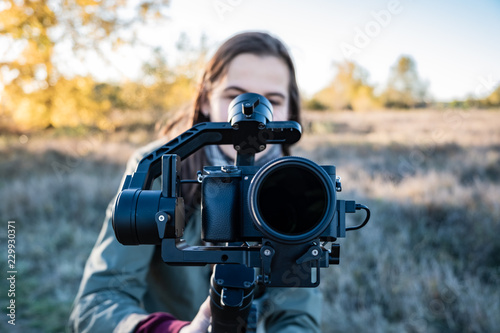 Female videographer holding a gimbal with mirrorless camera. Woman with stabilized camera rig filming outdoors on a sunny afternoon photo