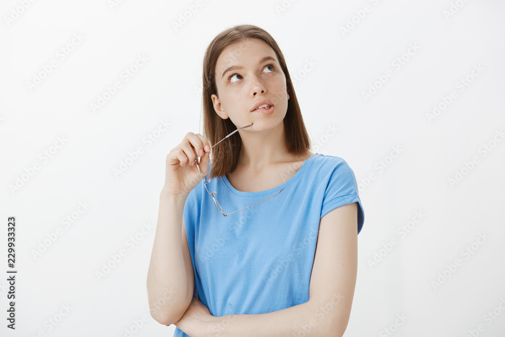 Girl dreaming, thinking how spend leisure. Portrait of smart good-looking european woman, biting rim of glasses, looking at upper right corner, being intrigued and interested in something Girl dreaming, thinking how spend leisure. Portrait of smart good-looking european woman, biting rim of glasses, looking at upper right corner, being intrigued and interested in something