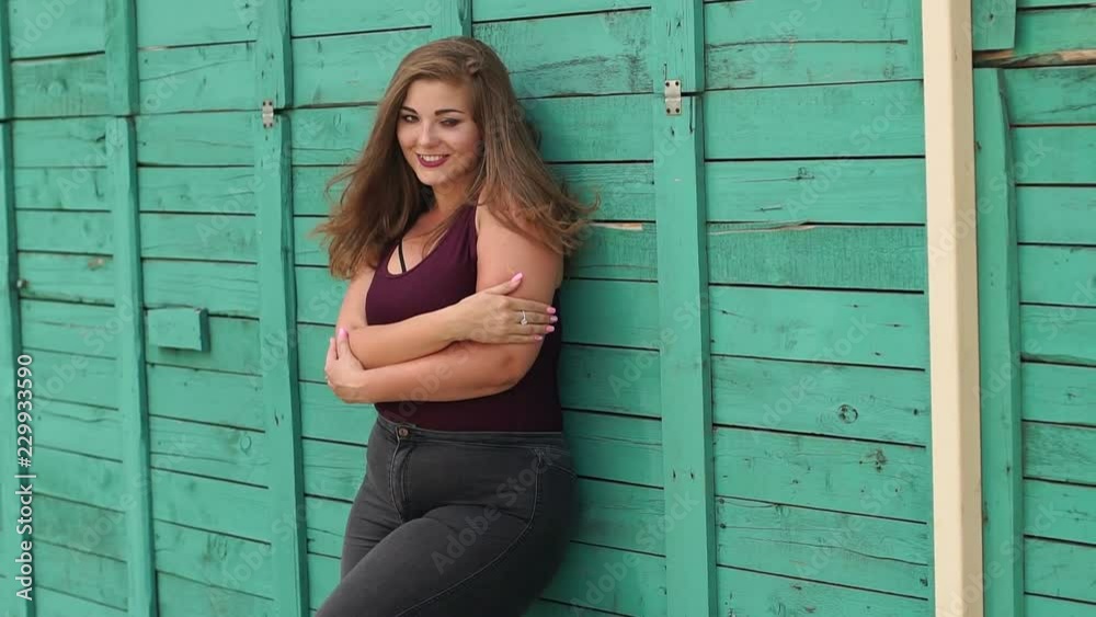 Smiling young girl with excess weight poses in the park on the background of the green wall. Plus size model. Smiling young girl with excess weight poses in the park on the background of the green wall. Plus size model.