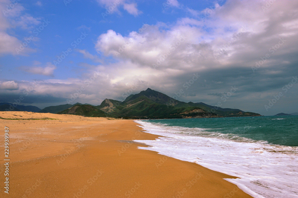 Empty vast sandy beach in Quy Nhohn, Vietnam. Mountains in the background, yellow sand and partly cloudy sky. Empty vast sandy beach in Quy Nhohn, Vietnam. Mountains in the background, yellow sand and partly cloudy sky.