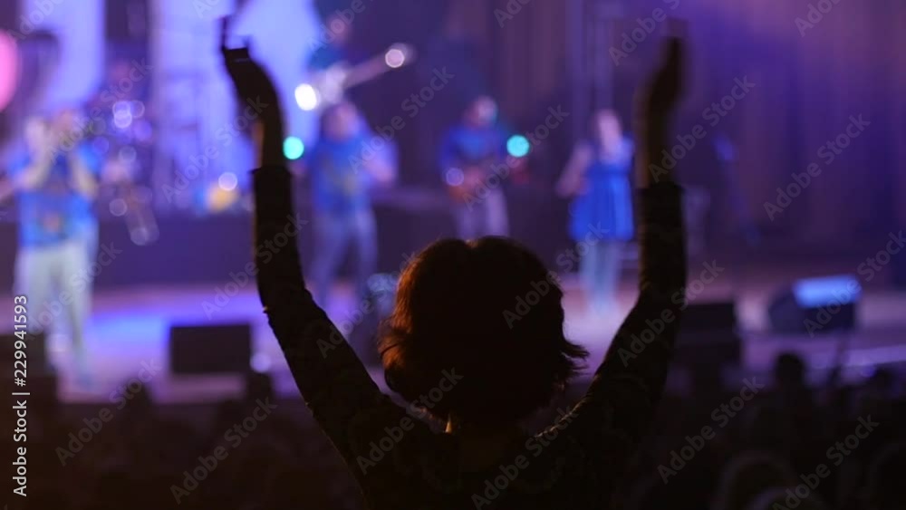 Dancing girl fan silhouettes on a concert flashing light cheerful hands in air