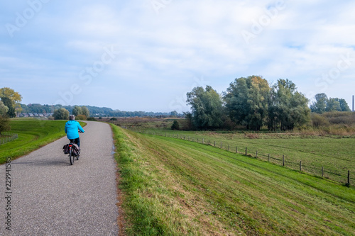 Woman on a bicycle on the dike along the flood plains along the river Nederrijn in Wageningen, the Netherlands. © FotoCorn