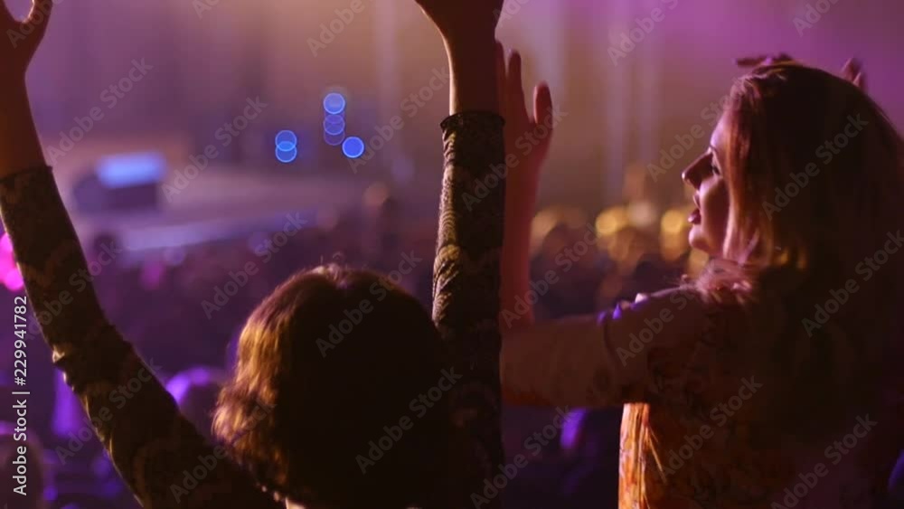 Dancing girl fan silhouettes on a concert flashing light cheerful hands in air