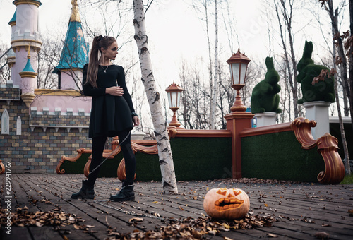 A girl with beautiful make-up walks a hand-pumpkin on a leash in a fabulous park. Halloween creative picture