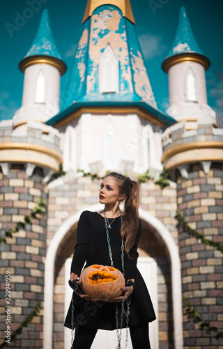 A girl with beautiful make-up walks a hand-pumpkin on a leash in a fabulous park. Halloween creative picture