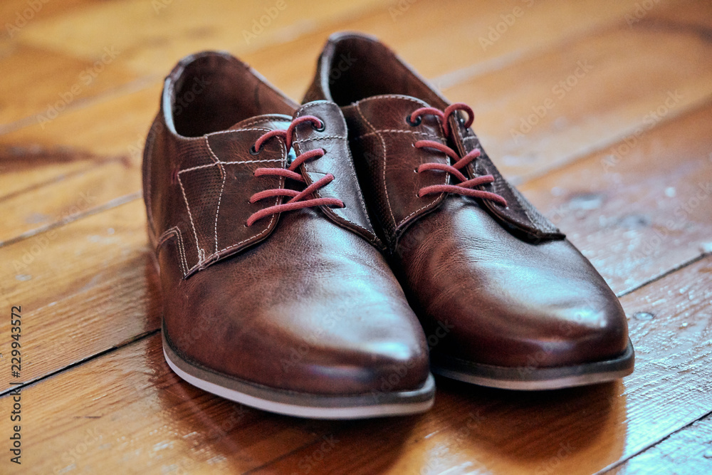 Brown leather shoes of a groom with red shoe laces on a wooden floor Brown leather shoes of a groom with red shoe laces on a wooden floor