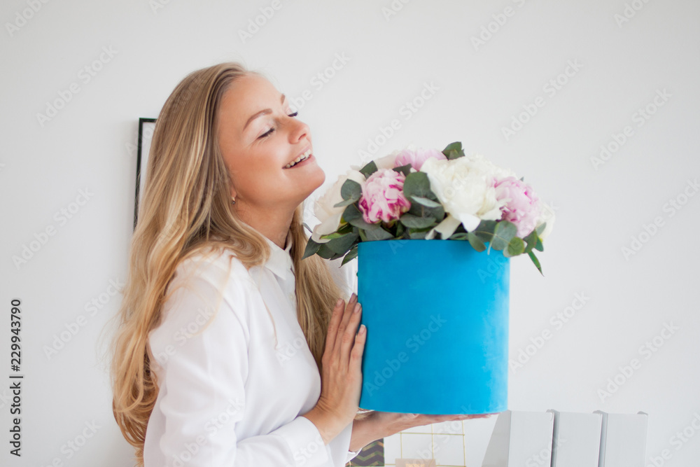 Stylish young blonde in office, white shirt and pants. Holds a luxurious bouquet of peonies in a blue hat box. Stylish young blonde in office, white shirt and pants. Holds a luxurious bouquet of peonies in a blue hat box.