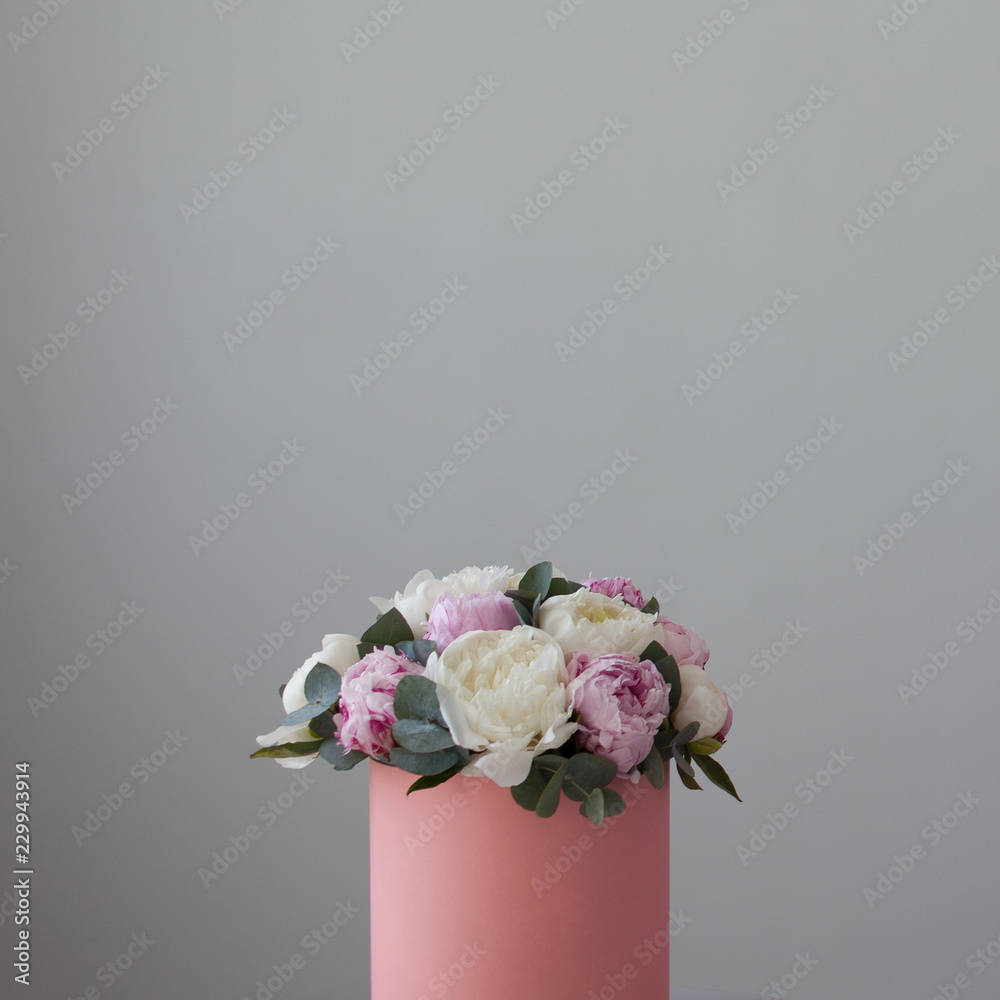 chic bouquet of peonies in a gift hat box. Pink box on light grey background