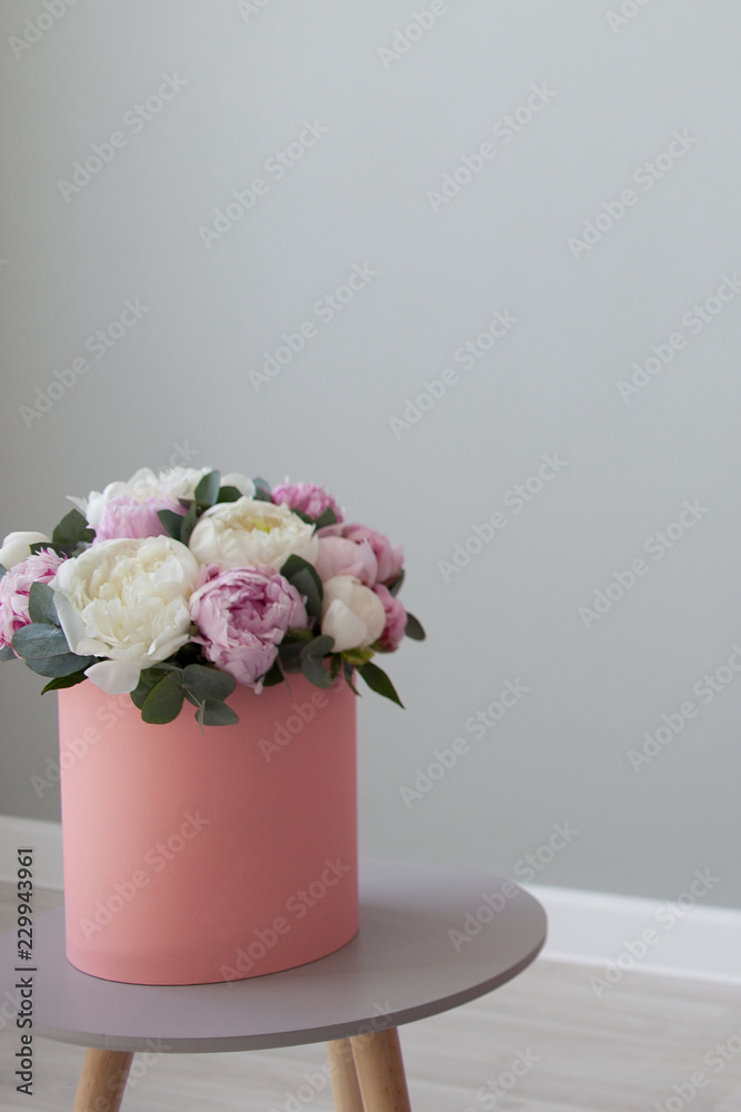 chic bouquet of peonies in a gift hat box. Pink box on light grey background