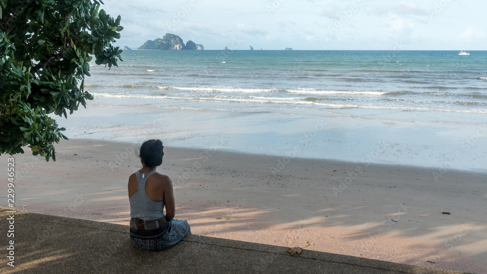 Fototapeta premium Woman sitting on sidewalk at beach looking at islands