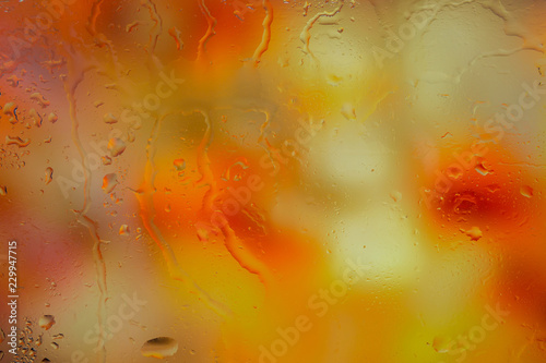 Autumn background. Drops of rain on the wet window and autumn colors of red orange and yellow. Blurred abstract texture background.