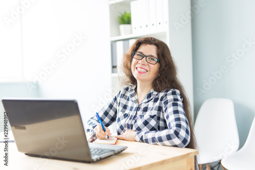 Business and people concept - Young smiling woman sitting in office and working