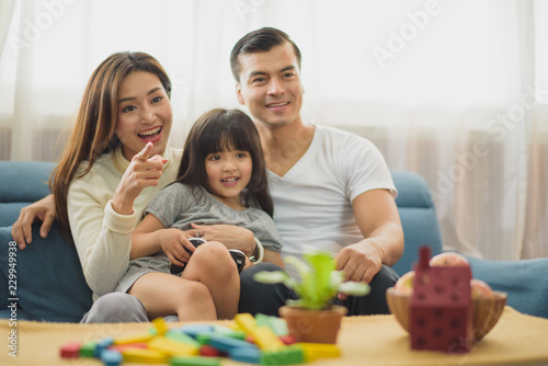 Family time young Parents and Daughter laughing which sit on sofa, daughter sit between father and mother and looking TV at home
