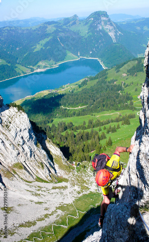 rock climber on a steep climb in the Swiss Alps above a beautiful turquoise mountain lake photo