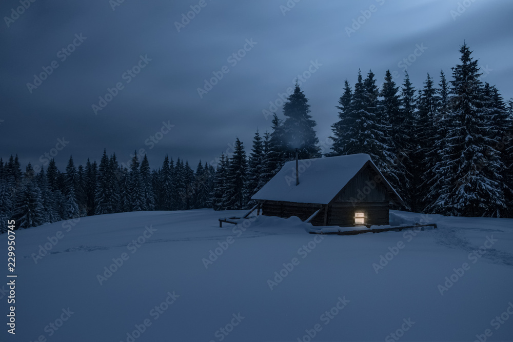 Wooden cabin under stars. Lights shines through the window from inside of the house. Night landscape in winter.