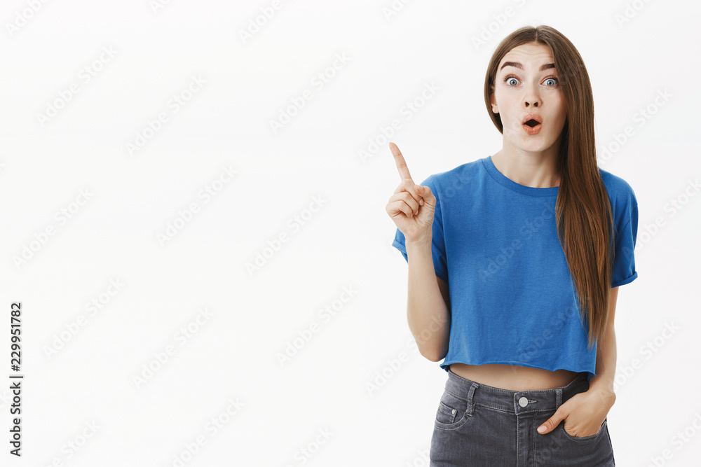 Waist-up shot of creative european female employee adding great idea raising index finger in eureka gesture folding lips talking with excitement and joy about own plan adding suggestion over grey wall Waist-up shot of creative european female employee adding great idea raising index finger in eureka gesture folding lips talking with excitement and joy about own plan adding suggestion over grey wall