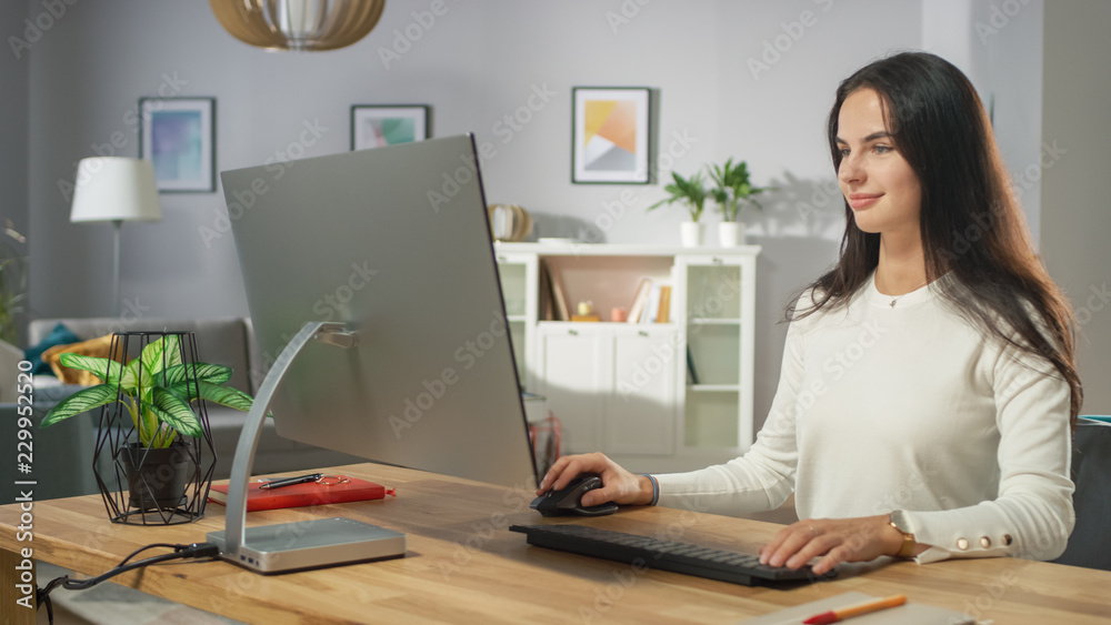 Portrait Shot of the Beautiful Young Woman Working on Personal Computer from Her Cozy Living Room. She Smiles Charmingly.