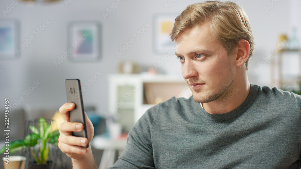 Portrait of the Handsome Young Man Using Smartphone, Browsing in Internet, Checking Social Networks while Sitting At Home. Portrait of the Handsome Young Man Using Smartphone, Browsing in Internet, Checking Social Networks while Sitting At Home.