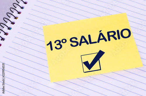 Sheet of yellow post note paper or self-adhesive notes written 13º salary (in portuguese)with background notebook. photo