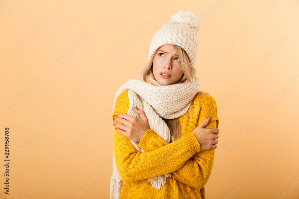 Displeased frozen woman wearing scarf and hat posing isolated over yellow wall background. Displeased frozen woman wearing scarf and hat posing isolated over yellow wall background.