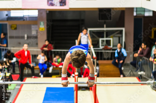 Little child athletic gymnast performing exercises at the bar in the championship