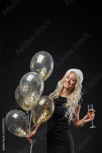 Young woman in Santa Clause hat with a champagne glasses at celebration with balloons on black background