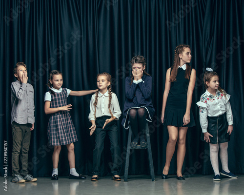 Cute surprised stylish children on dark background. Beautiful stylish teen girls and boy standing together and posing on the school stage in front of the curtain. Classic style. Kids fashion and