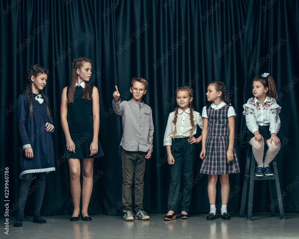 Cute surprised stylish children on dark background. Beautiful stylish teen girls and boy standing together and posing on the school stage in front of the curtain. Classic style. Kids fashion and