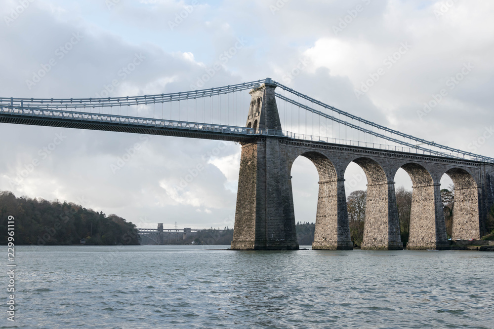 A view of the historic Menai suspension bridge spanning the Menai Straits, Gwynnedd, Wales, UK. A view of the historic Menai suspension bridge spanning the Menai Straits, Gwynnedd, Wales, UK.