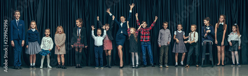 Cute smiling happy stylish children and female teacher on pink background. Beautiful stylish teen girls and boy standing together and posing on the school stage in front of the curtain. Classic style