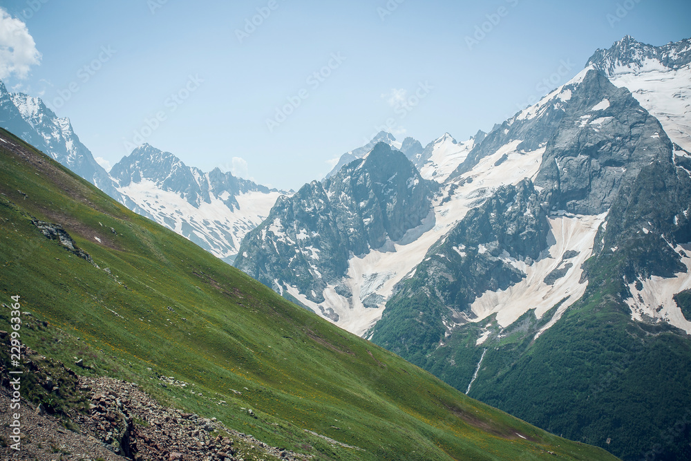 Mountain lawn with green grass on the background of snowy peaks of the Caucasus mountains, summer Sunny day