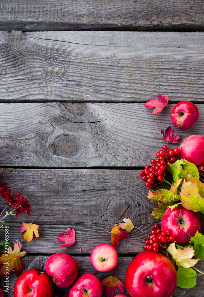 Many red apples lie on a wooden background, autumn colored, yellow leaves, viburnum, September, October, November, the background for the inscription, the frame for the signature Many red apples lie on a wooden background, autumn colored, yellow leaves, viburnum, September, October, November, the background for the inscription, the frame for the signature