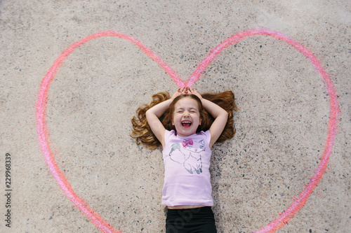 Cute young girl laying in a chalk drawn heart on the ground