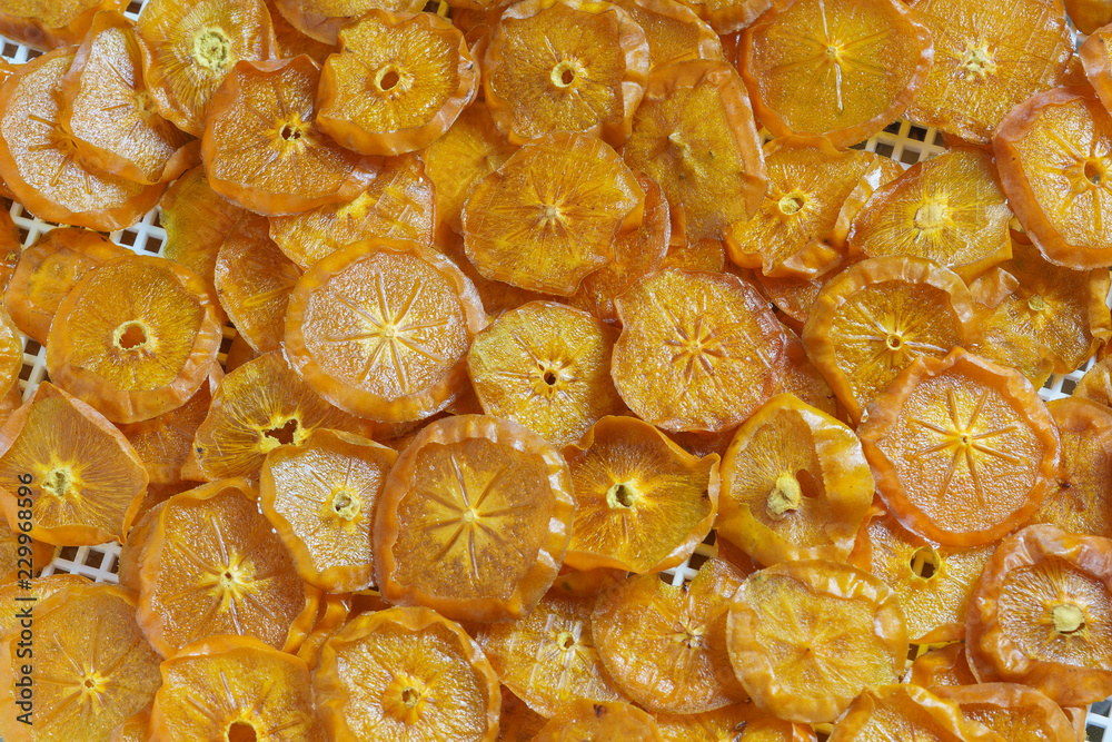 Orange background of dried persimmon slices laid out on the white grid of the electric dryer Orange background of dried persimmon slices laid out on the white grid of the electric dryer