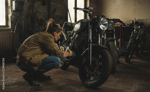 Young female working on restoration of old /vintage motorbikes in old rusty motorbike garage/workshop