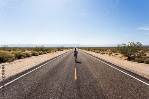A young woman running down a long straight stretch of road in the desert photo