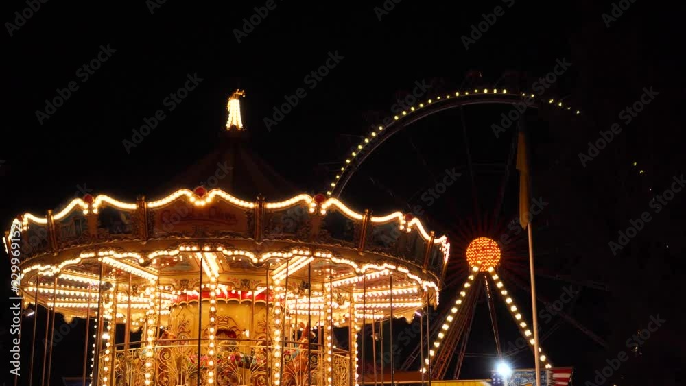 Beautiful flashing lights of retro merry go round carousel night illumination of big ferris wheel in amusement park fair