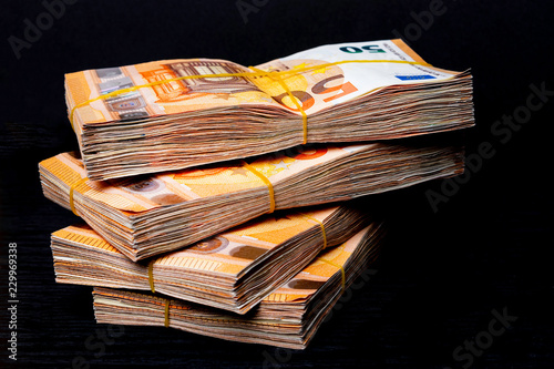 Pile of 50 real euro notes 50-euro banknotes under rubber band isolated on black. About 20000 euros worth.
