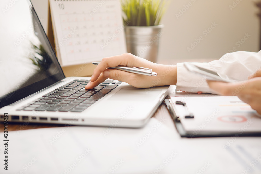 woman hand working with smart phone and laptop on desk in office in morning light woman hand working with smart phone and laptop on desk in office in morning light
